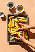 Female hands mixing sliced raw potatoes with salt, olive oil and dried herbs