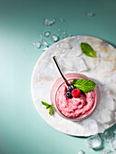 Berry and mint smoothie on a marble tray with ice on a pastel green surface.