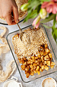 Spooning crumble topping mixture over a baking dish holding pineapple chunks