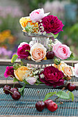 Etagere mit Rosenblüten, Wiesenkümmel, Samenkapseln von Jungfer im Grünen und Süßkirschen