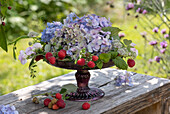 Summer arrangement with hydrangea blossoms, raspberries, crownvetch, and starflower on a pedestal