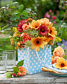 Summer bouquet in fiery colors: Dahlia 'Mystic Spirit', roses, sneezeweed, Queen Anne's Lace, yellow raspberry 'Golden Bliss', golden Marigold and yellow Galium in dotted gift bag