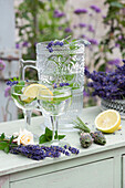 Krug und Gläser mit Wasser, Minze und Zitrone als Erfrischungsgetränk, Rosenblüte, Lavendelblüten und Lavendelflaschen