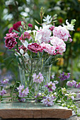 Small bouquet of carnation blossoms and magnificent candle, tendrils of crown vetch in front of it