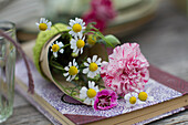 Kleine Blütendekoration mit Nelkenblüten und Kamille in selbstgemachter Spitztüte aus Papier