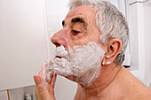 Elderly man shaving in front of a bathroom mirror