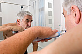 Elderly man using an electric toothbrush to clean his teeth