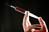 Hand gently squeezing a hypodermic syringe