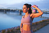 Young woman holding kettlebell on shoulder at riverbank