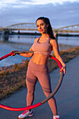 Young sporty woman holding hula hoop at riverbank