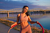 Athlete woman holding hula hoop at riverbank
