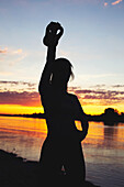 Young woman silhouette holding kettlebell at riverbank