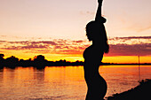 Silhouette of a woman with arms up at a riverbank