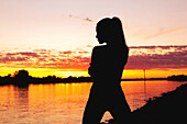 Silhouette of a woman at a riverbank at sunset