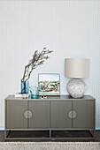 Vase, picture and table lamp on sideboard with fluted doors