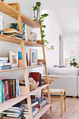 Offenes Bücherregal aus hellem Holz, daneben Stuhl und Sofa in offenem Wohnraum