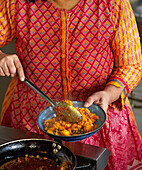 Indische Frau bereitet Garnelencurry mit Erbsen zu