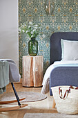 Tree trunk bedside table next to double bed in front of wallpapered wall in bedroom