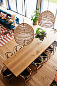 View down onto long dining table with chairs and rattan lamps in open-plan interior