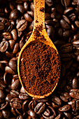 A wooden spoon holding ground coffee in a backdrop of roasted coffee beans