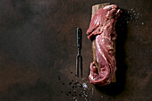 Fresh whole raw beef tenderloin on wooden board with metal meat fork