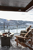 View from the balcony with outdoor chairs and glass balustrade to the snow-covered landscape