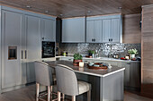 Custom kitchen cabinets with light grey fronts and kitchen island with upholstered chairs in the foreground