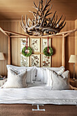 Double bed with wooden frame below antler chandelier in wood-panelled bedroom