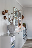 Vase of branches on sideboard below monkey head sculptures and photos on wall