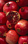 Whole pomegranates surrounding a pomegranate cut in half exposing the seeds