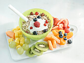 Bowl of oats, berries, and yogurt, on a plate with fruit next to it
