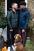 Happy gay male couple with dog on front stoop