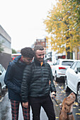 Gay male couple walking dog on wet autumn street