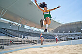 Female track and field athlete long jumping over sand
