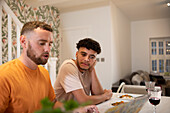 Gay male couple eating and using laptop in kitchen