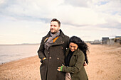 Happy couple in winter coats walking on beach