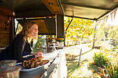 Happy female food cart owner in sunny autumn park