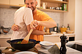 Happy gay male couple hugging and cooking in kitchen