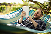 Happy man using digital tablet in sunny summer hammock