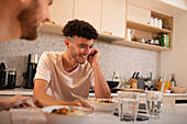 Happy young man eating and using laptop in kitchen