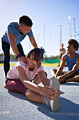 Happy young runners stretching on sunny sports track