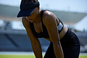 Tired female track and field athlete in visor resting