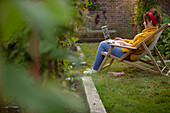 Woman working on laptop in lawn chair in summer garden