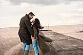 Happy affectionate couple in winter coats on beach
