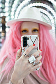 Woman with pink hair taking selfie with smart phone