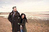 Affectionate couple in winter coats walking on beach