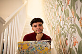 Confident young man with laptop on staircase at home