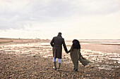 Couple in winter coats holding hands walking on beach