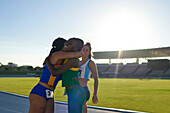 Female track and field athletes hugging on sunny track