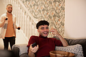 Happy young man with remote control watching TV on sofa
